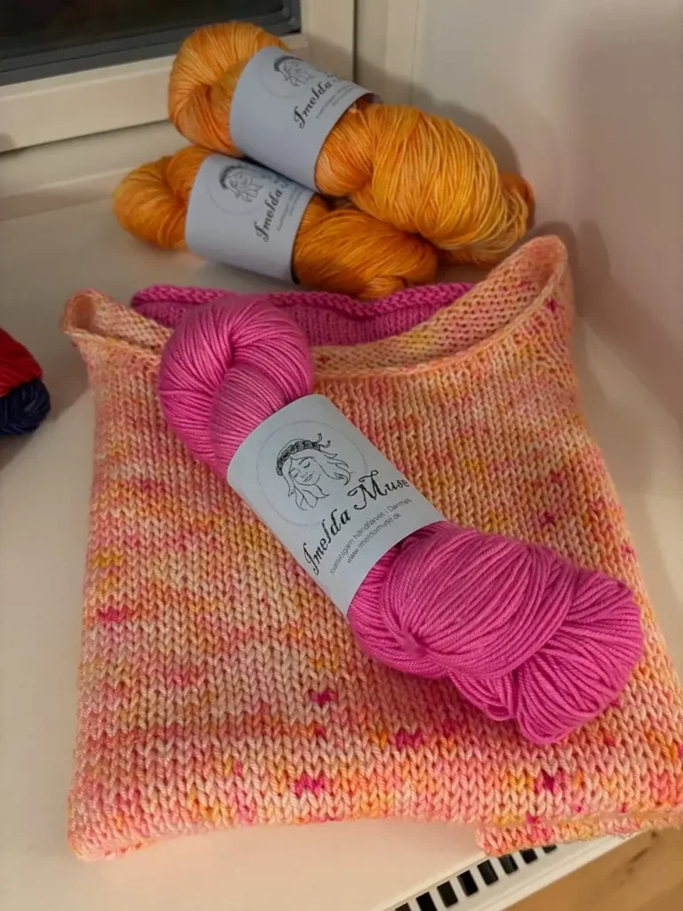 Håndfarvet garn i orange og pink på et strikket stykke