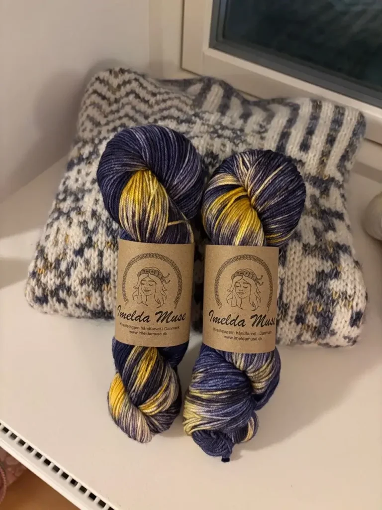 To fed håndfarvet garn i mørkeblå og gul på en strikket sweater